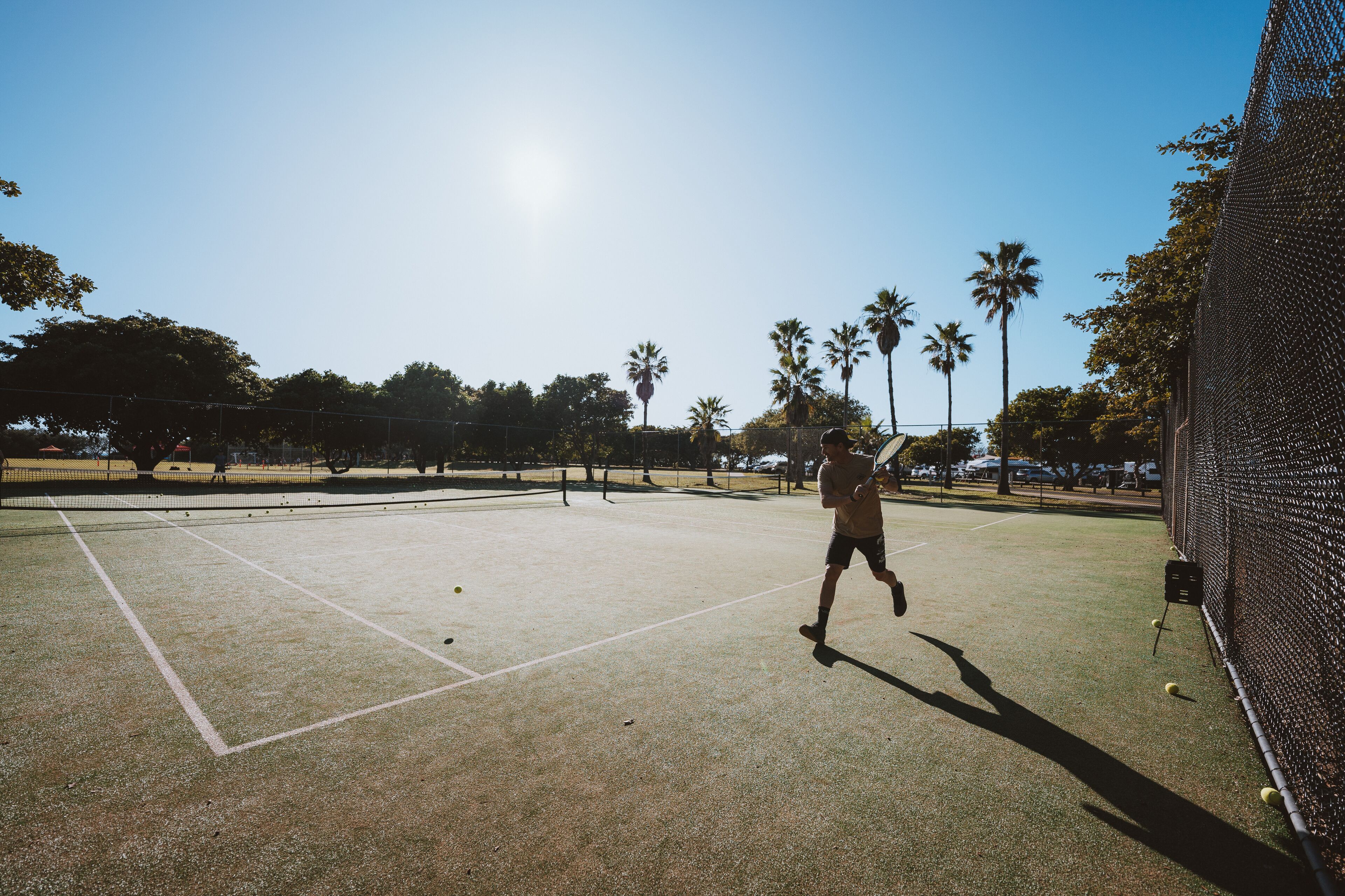 An outdoor tennis court with a net, surrounded by trees and a clear sky.