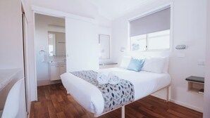 Ein Schlafzimmer mit einem Bett, einem Nachttisch, einem Fenster und einem durchgehenden Türspalt einsehbaren Badezimmer.
