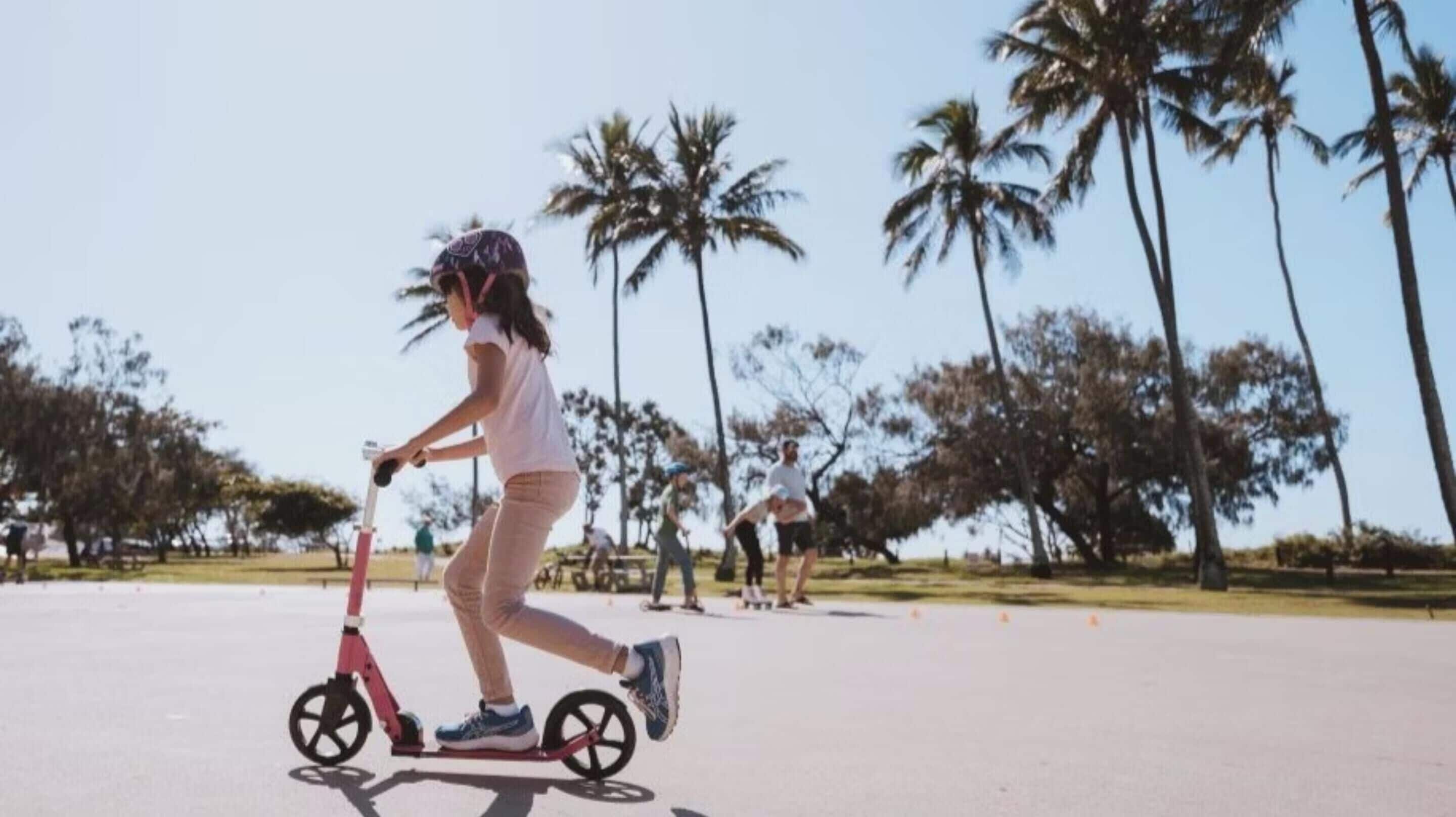 Iemand rijdt op een scooter over een verharde weg, met palmbomen op de achtergrond.