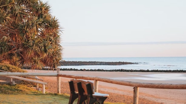 Blick auf einen Strand mit Holzlattenzaun, Stuhl und einer Palme.