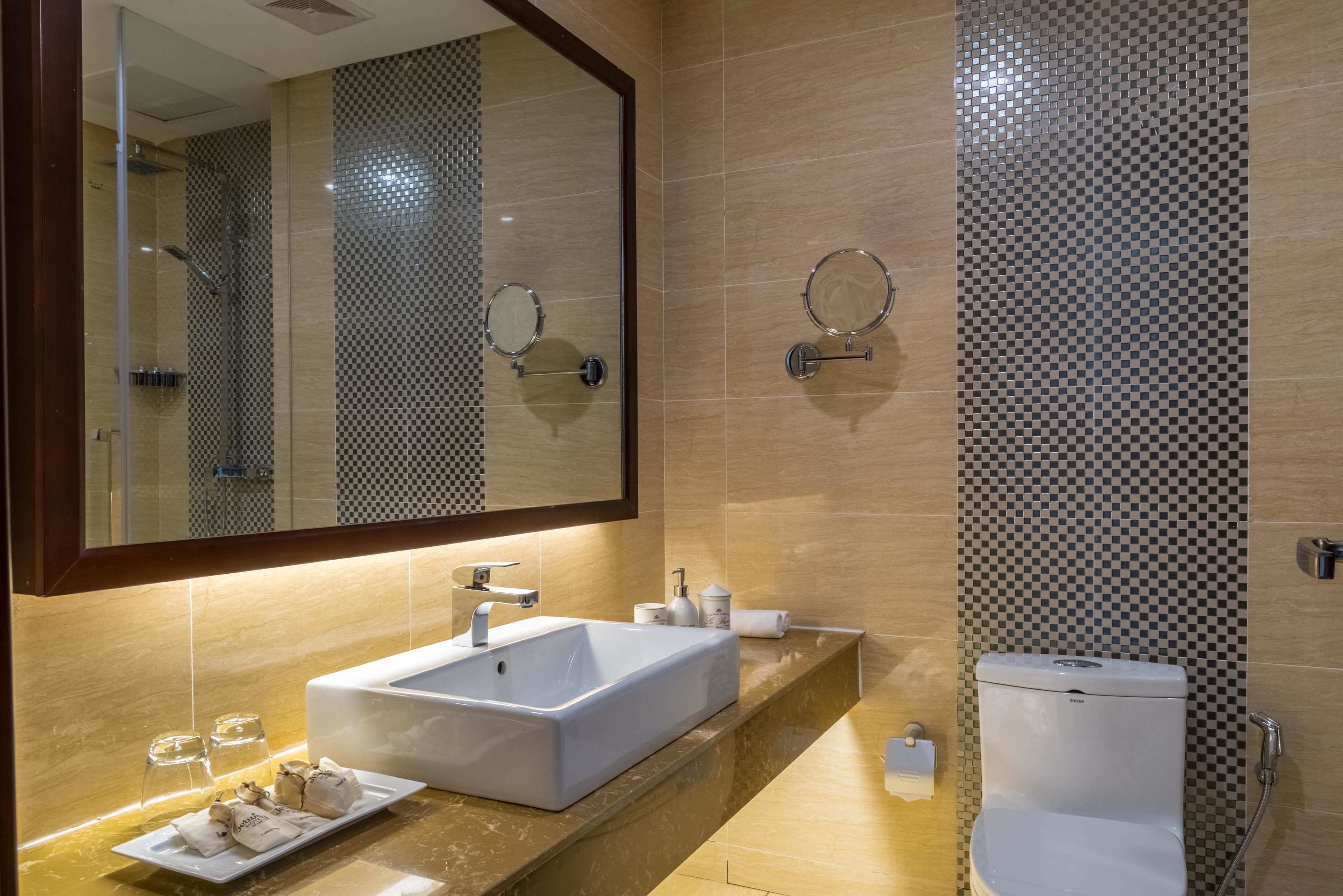 A modern bathroom with a large mirror, a white sink, a toilet, and a shower area.