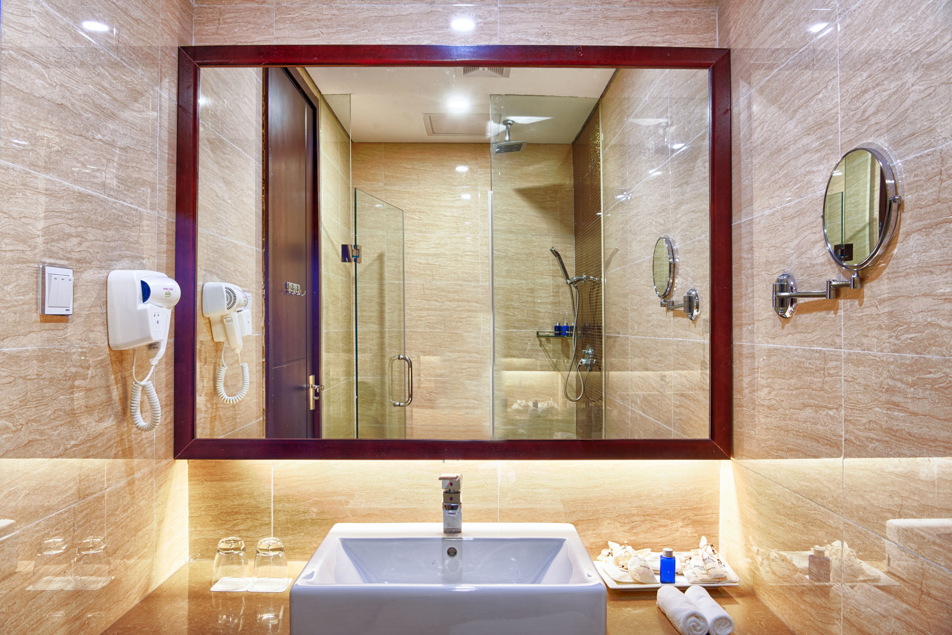 A modern bathroom with a large mirror, a sink, a shower, and a hairdryer.