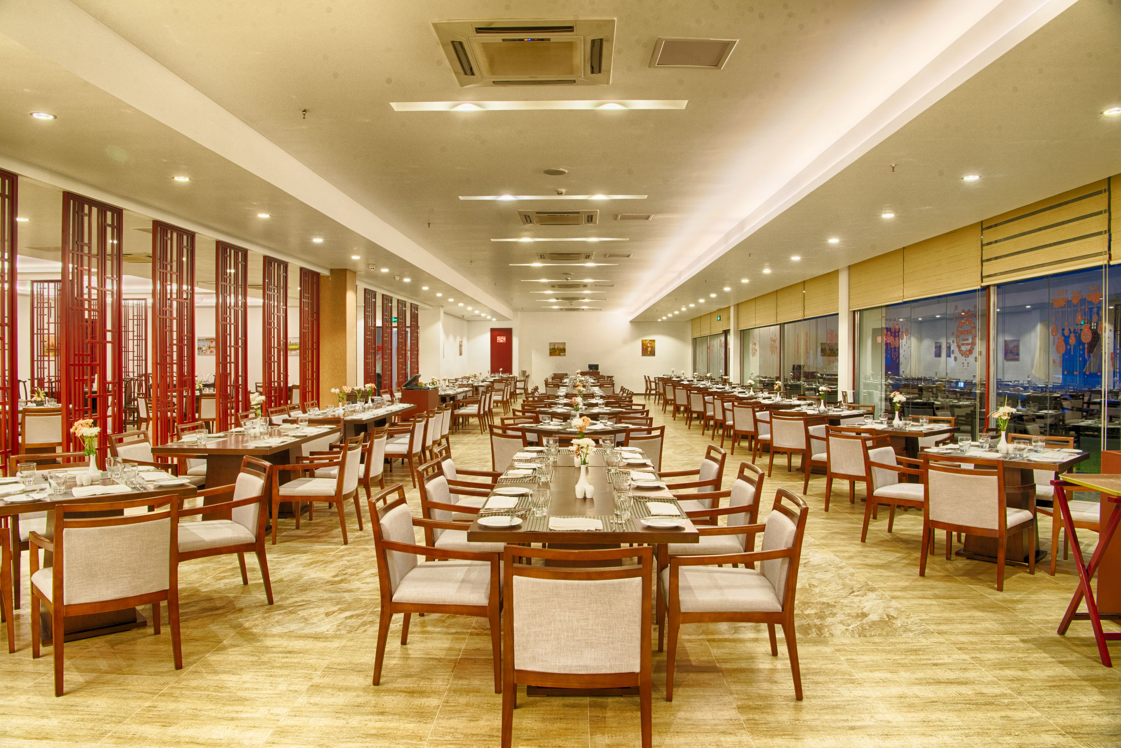 Un comedor espacioso con largas mesas y sillas, techos altos con iluminación empotrada y grandes ventanas que ofrecen vistas de la ciudad.