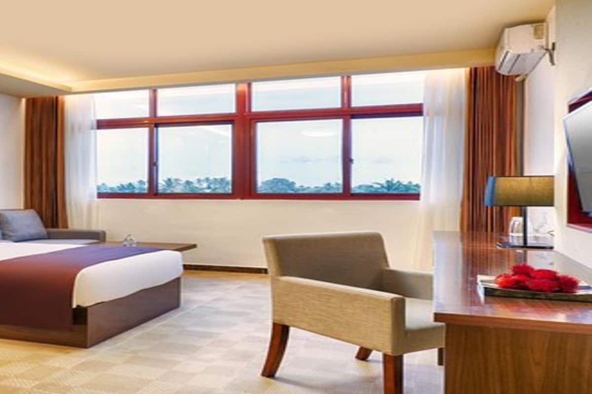 Habitación de hotel con dos camas, un escritorio, una silla y un ventanal con vistas.