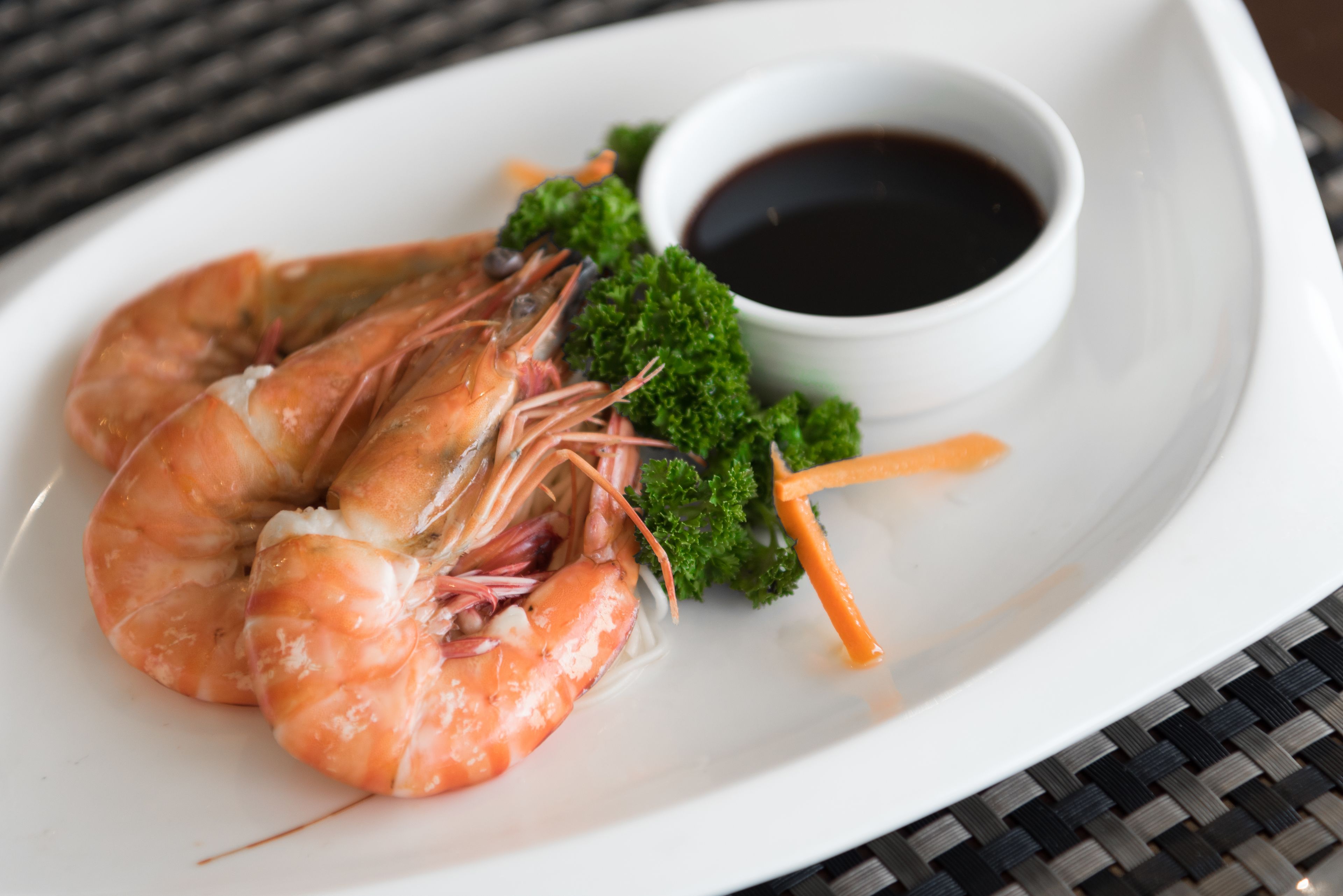 A plate with cooked shrimp, a small bowl of sauce, and some green garnish.
