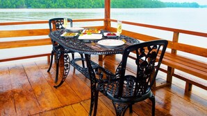 Une table à manger, dressée avec des assiettes de nourriture et des boissons, entourée de chaises, sur une terrasse en bois offrant une vue sur un lac et une forêt.