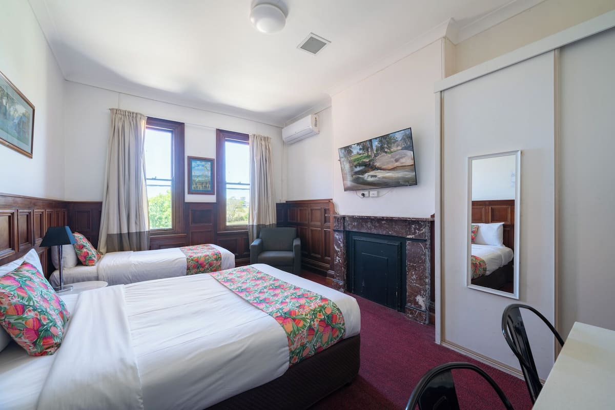 A hotel room with two beds, a fireplace, a TV, and a large window with curtains.