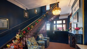 A grand staircase decorated with festive garlands, flanked by patterned armchairs and a chandelier. - The Hallows Accommodation (South Bathurst)