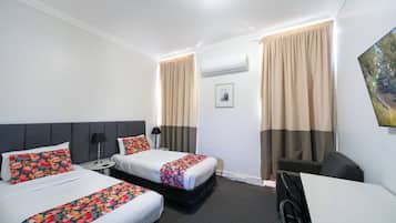 A hotel room with two beds, a desk, a wheelchair, and a painting on the wall.