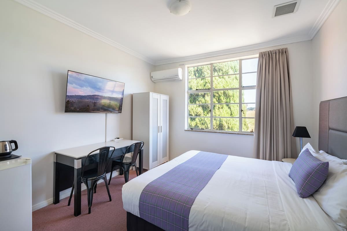 A hotel room with a bed, a desk, a chair, a television, and a window with curtains.