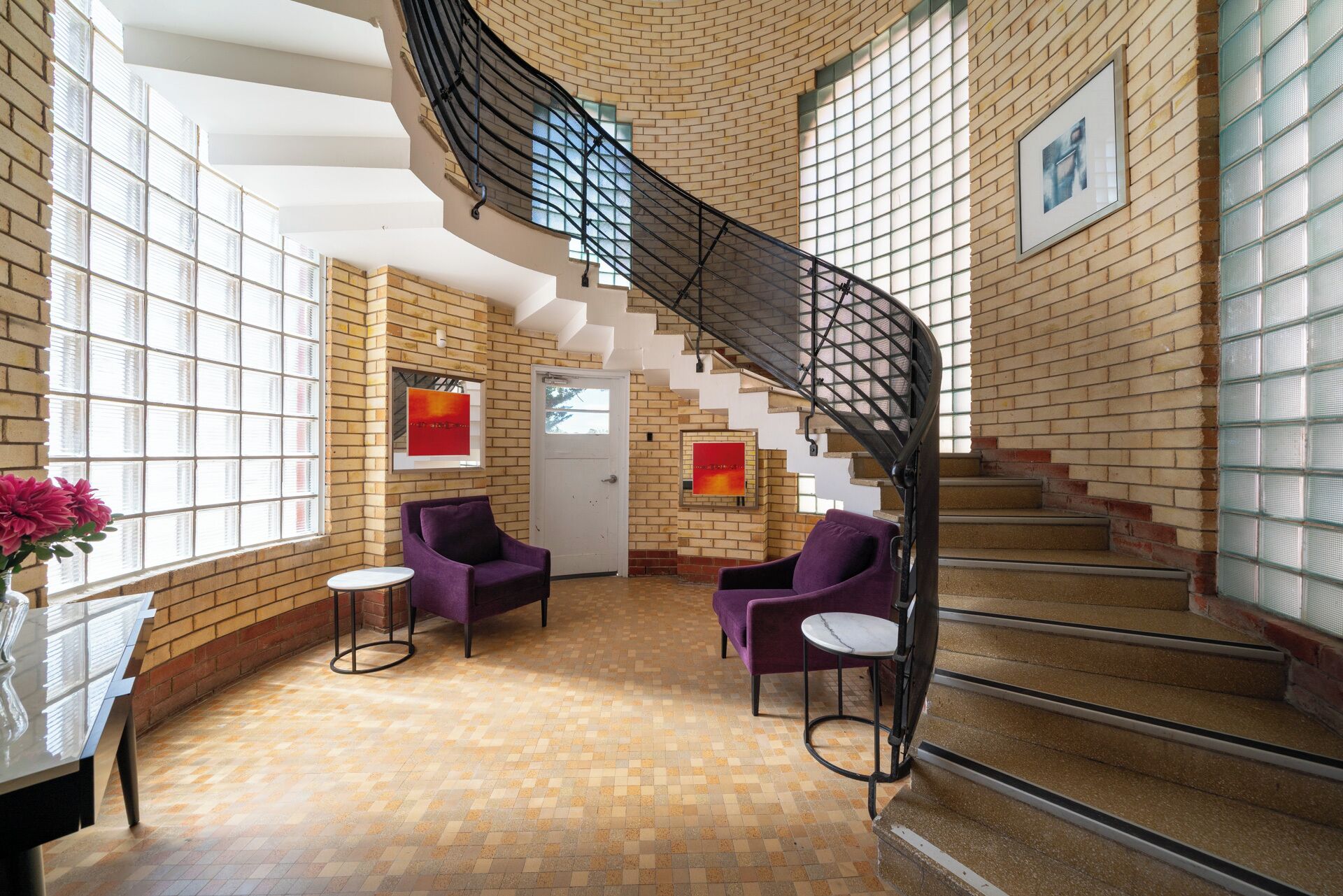 Un hall d’entrée spacieux avec un mur en briques, un escalier en colimaçon et deux fauteuils violets.