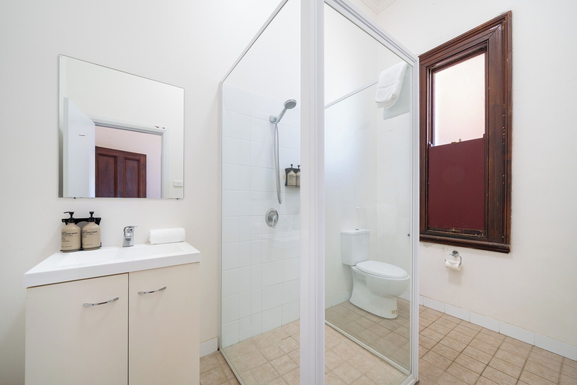 Et badeværelse med brusebad, toilet og et spejl over vasken.