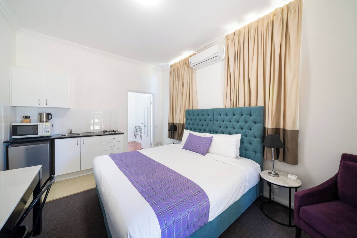 A hotel room with a bed, a desk, a kitchenette, and a bathroom.