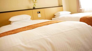 A hotel room with two beds, each with white linens and a brown throw blanket. There is a wall-mounted light fixture and a small plant on the wall. - Hotel Marix Lagoon (Miyazaki)