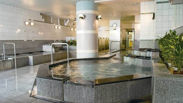 A modern indoor pool area with a central column, multiple seating areas, and a tiled floor. - Hotel Marix Lagoon (Miyazaki)