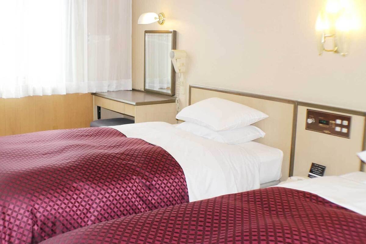 A hotel room with two beds, a desk, a mirror, and a TV.