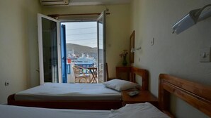A hotel room with two beds, a small table with chairs, a mirror, and a view of a ship through an open door. - Galaxy Hotel (Andros)