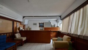 A spacious living area with a wooden reception desk, two sofas, a coffee table, and a vase with flowers. - Galaxy Hotel (Andros)