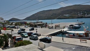 A coastal marina with parked cars, boats, and a clear view of the sea and hills in the background. - Galaxy Hotel (Andros)
