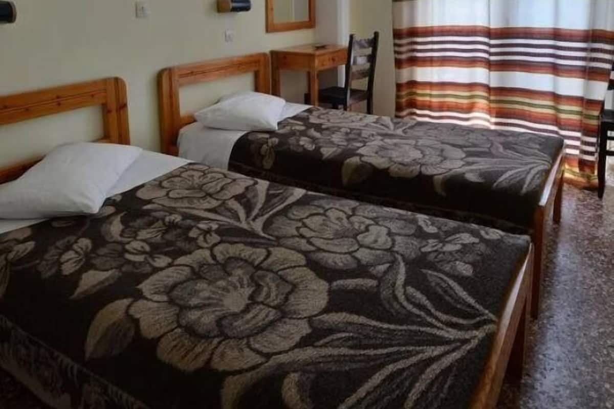 A room with two beds, a desk, a chair, and a window with curtains.