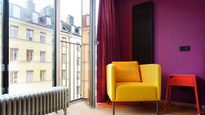 A room with a yellow chair, a red chair, a radiator, and a window with a view of buildings. - Hellstens Glashus (Stockholm)