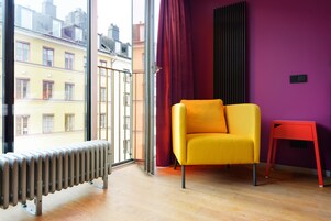 Una habitación con una silla amarilla, una silla roja, un radiador y una ventana con vistas a edificios.