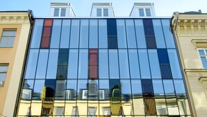 A modern building with large glass windows reflecting the sky and neighboring structures. - Hellstens Glashus (Stockholm)