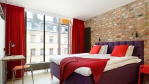 A modern bedroom with a purple bed, red curtains, and a brick wall. - Hellstens Glashus (Stockholm)