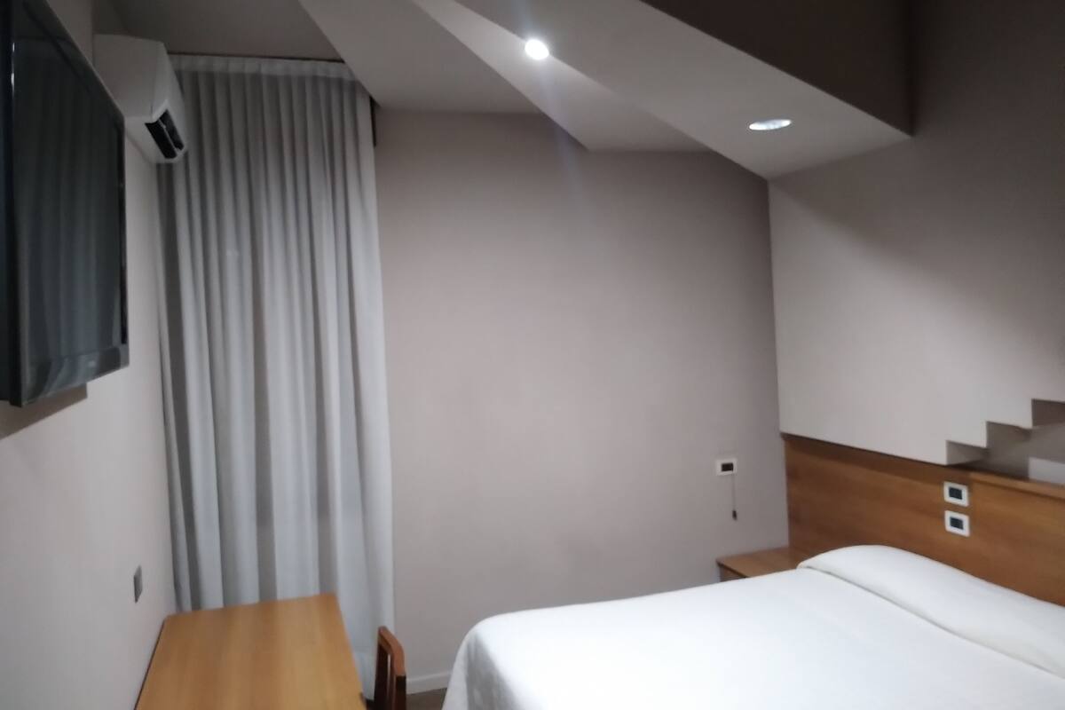 Une chambre d’hôtel avec un lit, un bureau, une chaise, une télévision et un escalier.
