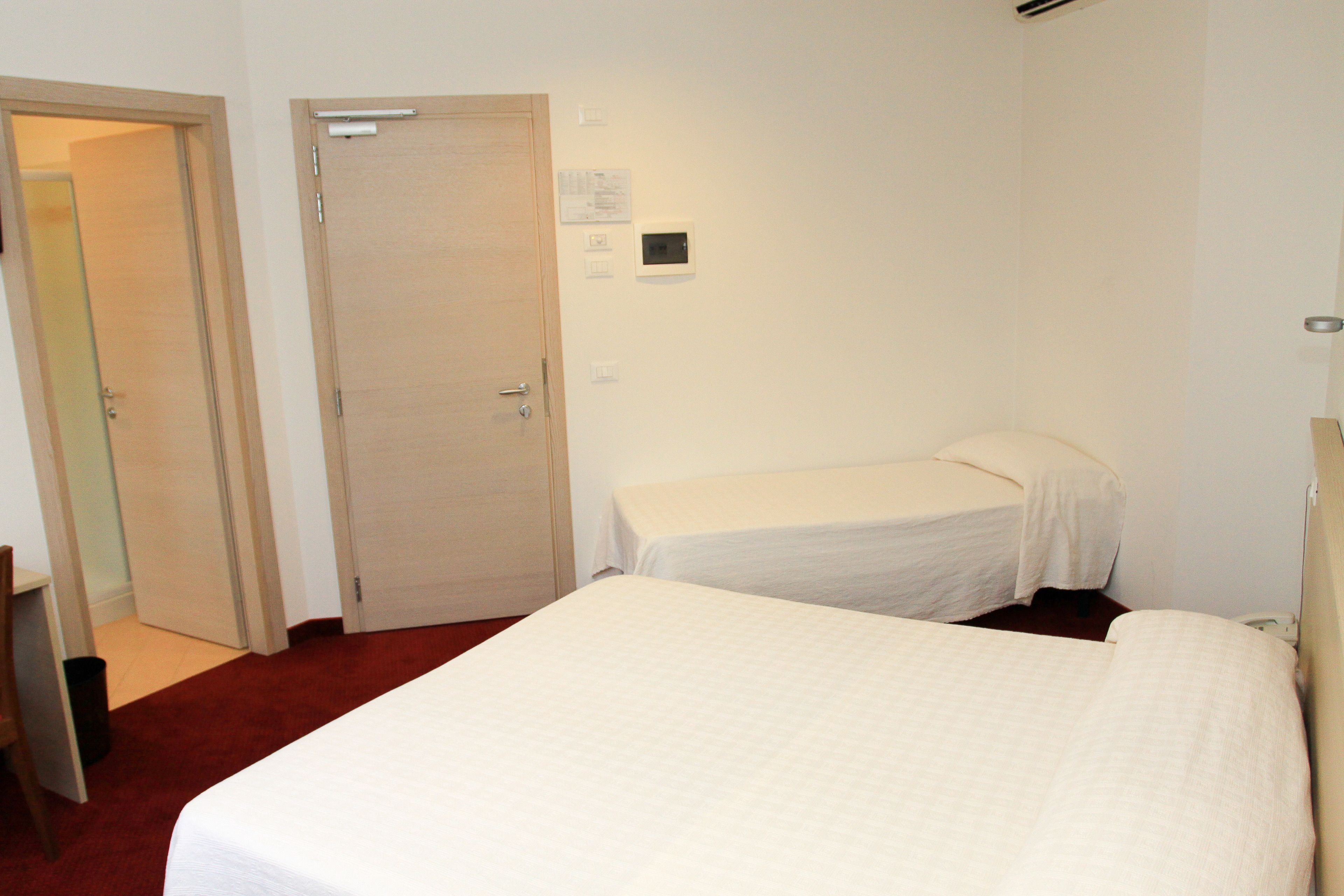 Camera d'albergo con due letti, una porta e un piccolo cestino.