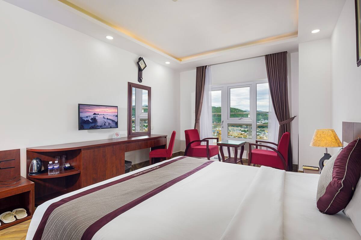 A hotel room with a bed, a desk, a chair, a TV, and a window with a view.