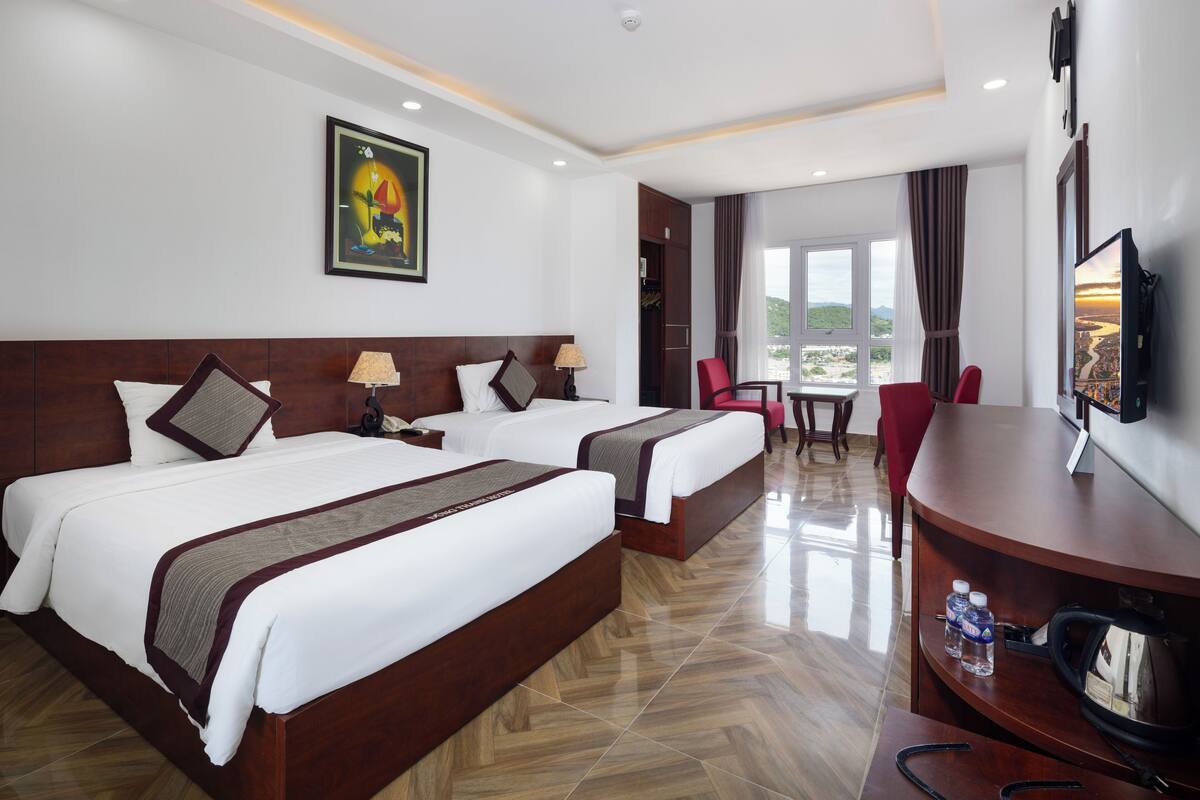 A hotel room with two beds, a desk with a television, and a view of the outdoors.