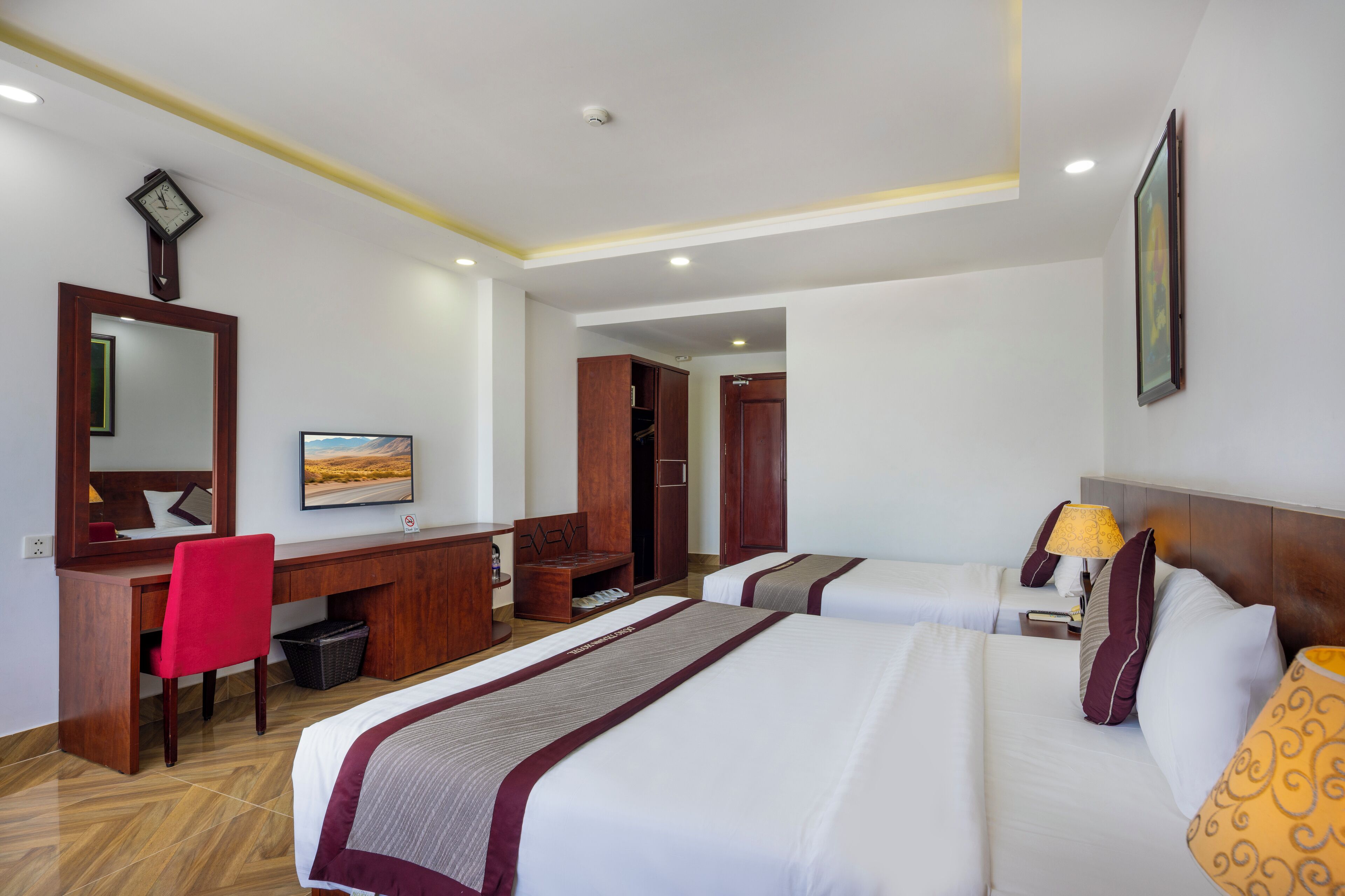 A hotel room with two beds, a desk, a chair, a wardrobe, and a mirror.