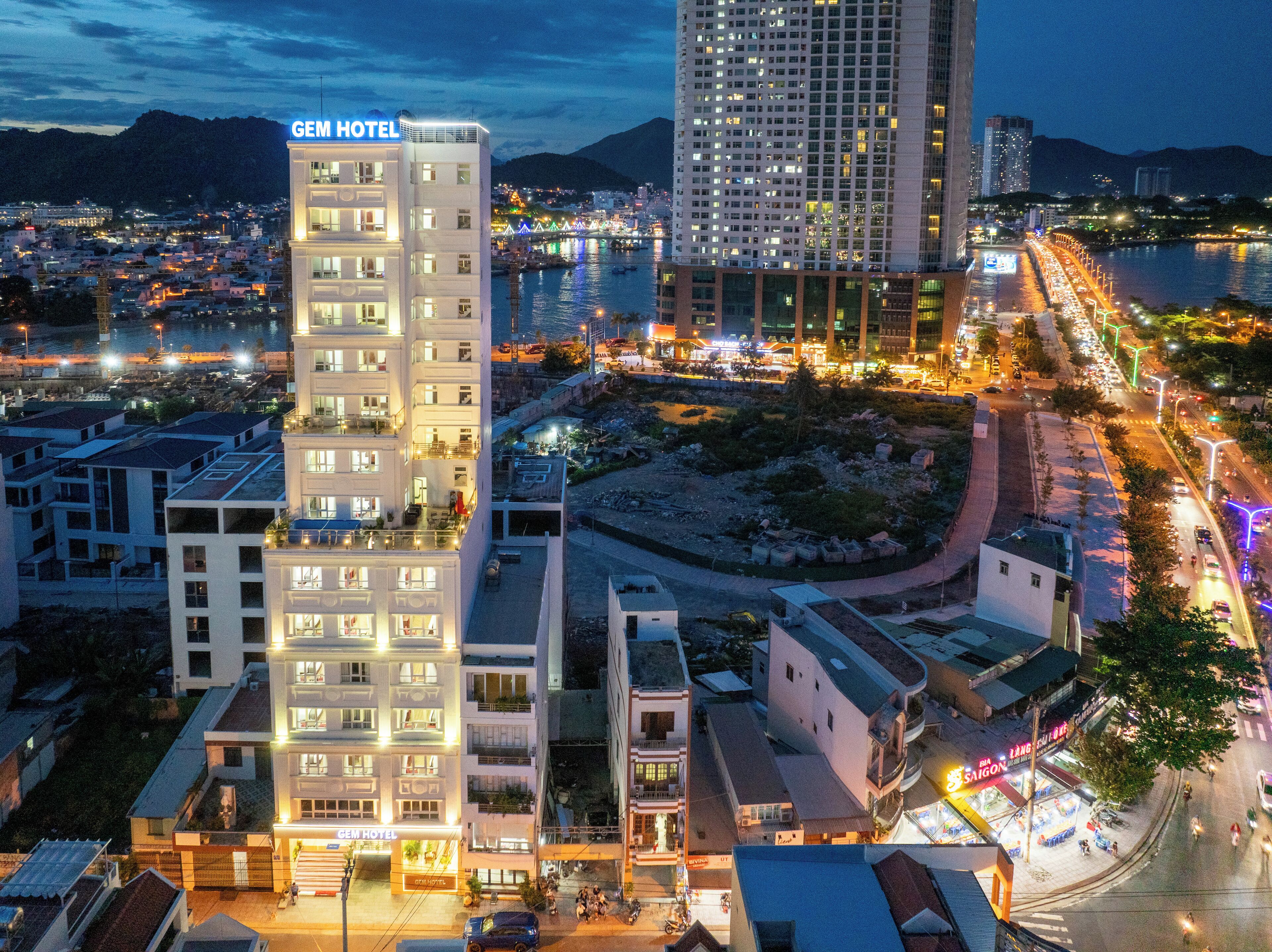 A multi-story hotel with a prominent 'Gem Hotel' sign, surrounded by urban buildings and a waterfront.
