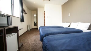 Et hotelværelse med to senge, et skrivebord med computer, fjernsyn og et lille køleskab.