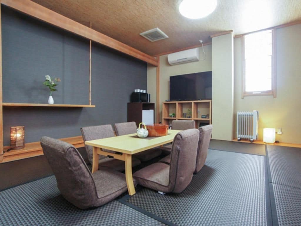 A room with a wooden ceiling, a flat-screen TV, a table with chairs, a radiator, and a window.