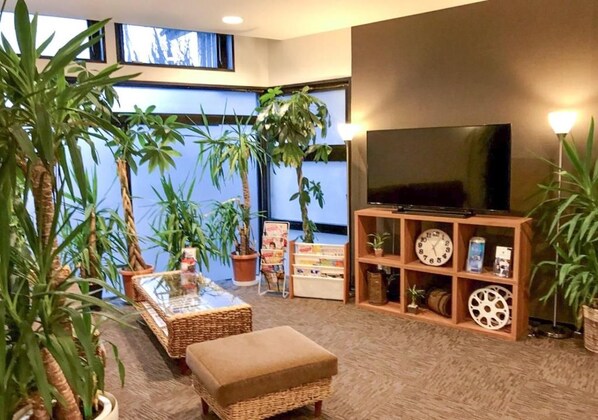 A living room with a television, a bookshelf, and several potted plants. - HOTEL LiVEMAX Gunma Numata (Numata)