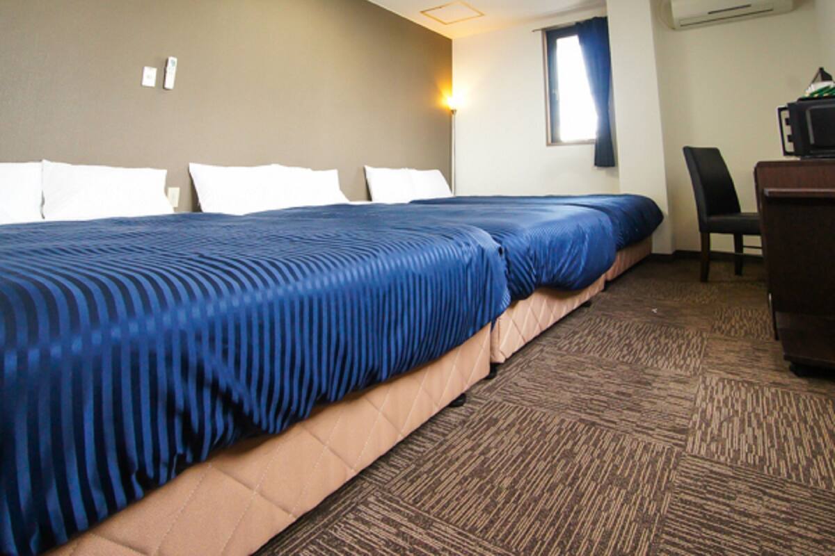 A hotel room with a large bed, a desk, and an air conditioning unit on the wall.