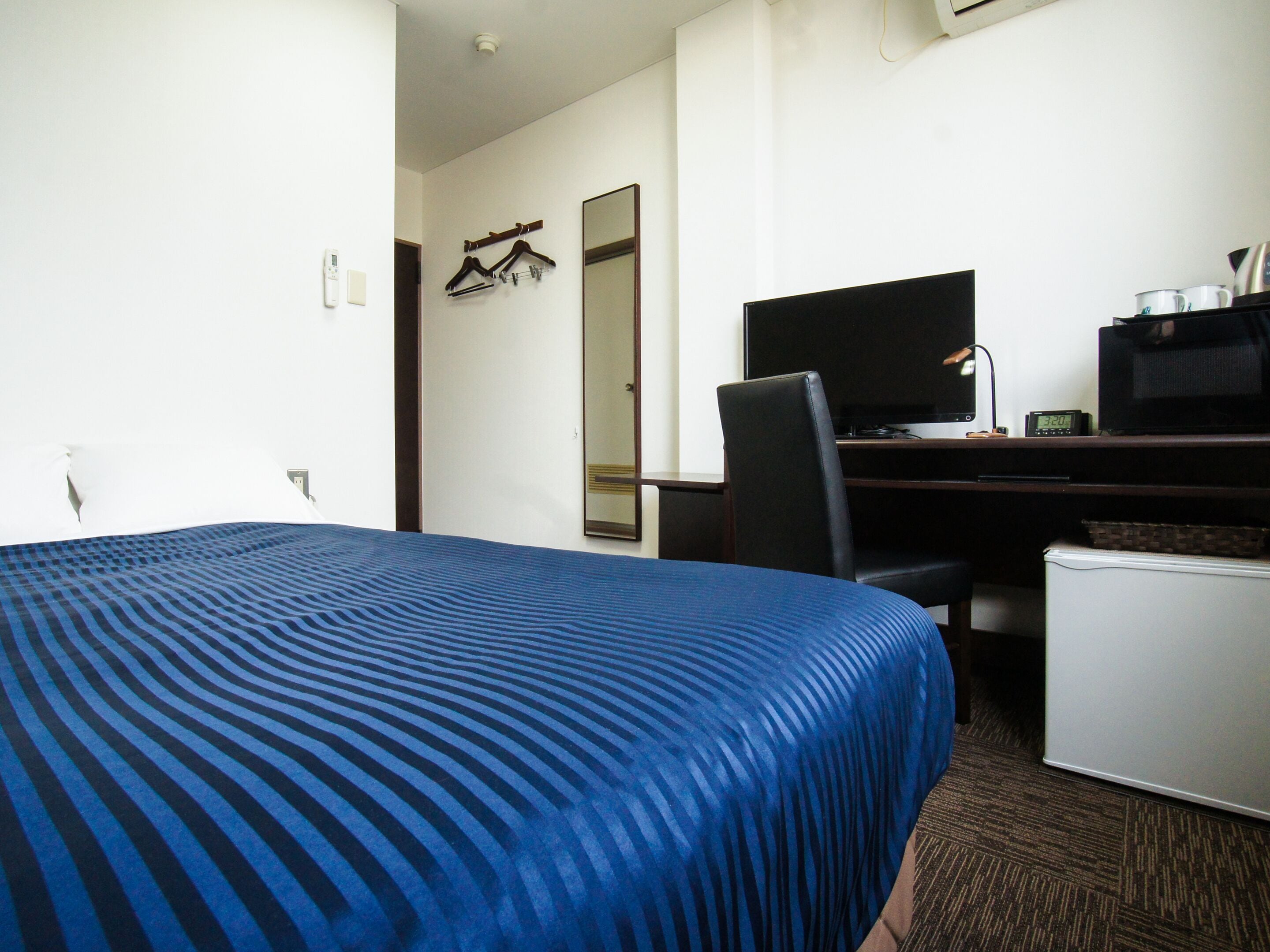 Una habitación de hotel con cama, escritorio con computadora, silla y microondas.