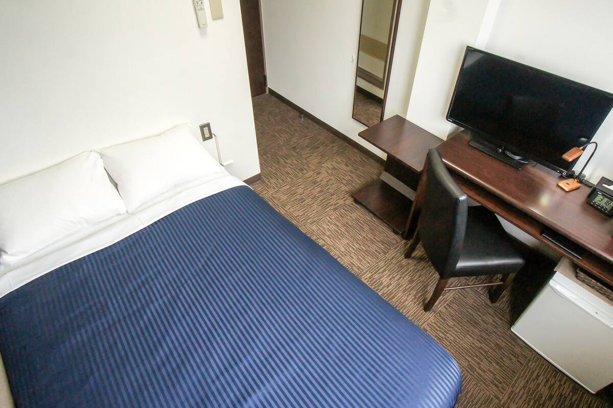 A hotel room with a bed, a desk, a chair, a television, and a small refrigerator.