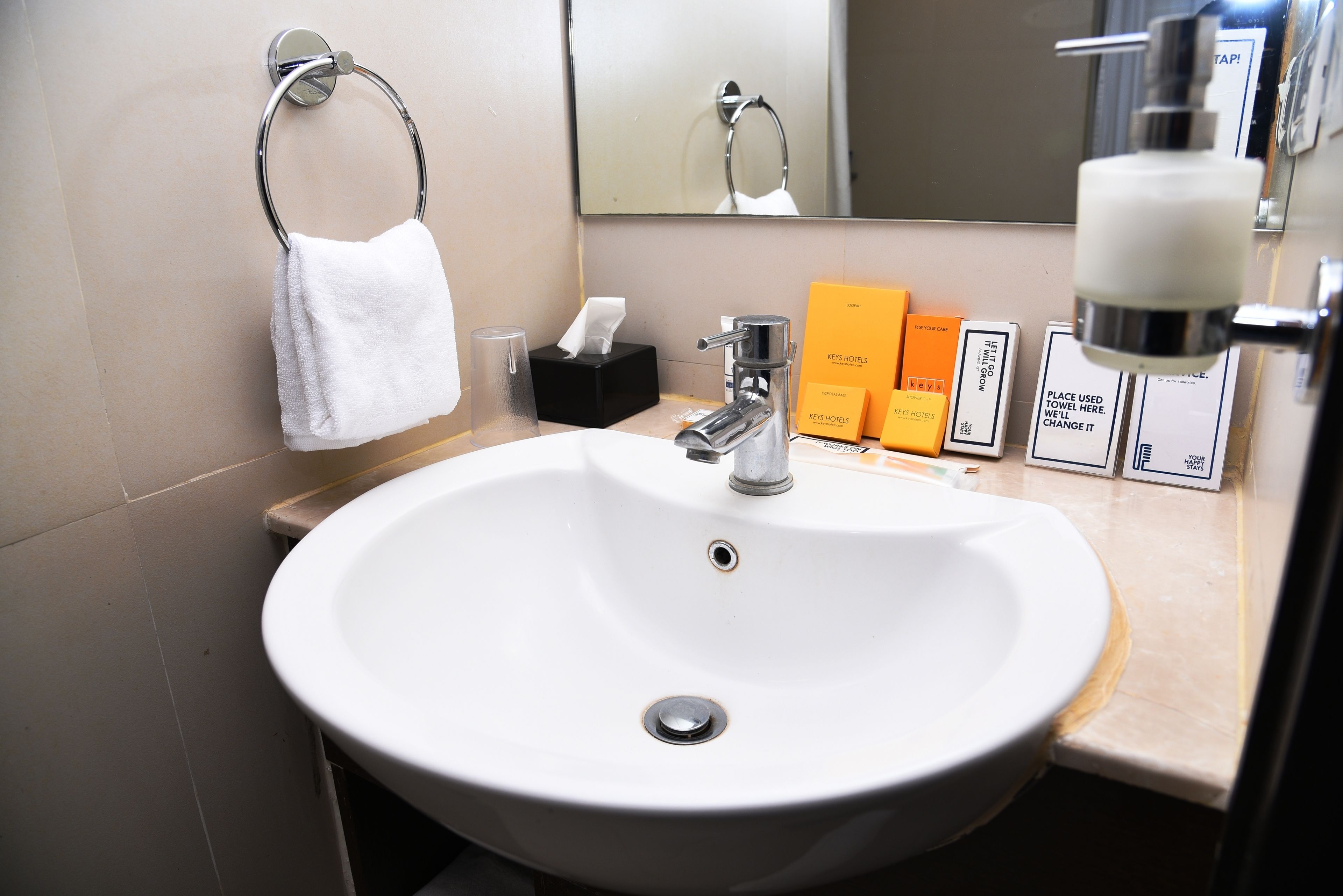 Un baño de hotel con un lavamanos blanco, toallero, espejo y artículos de aseo.
