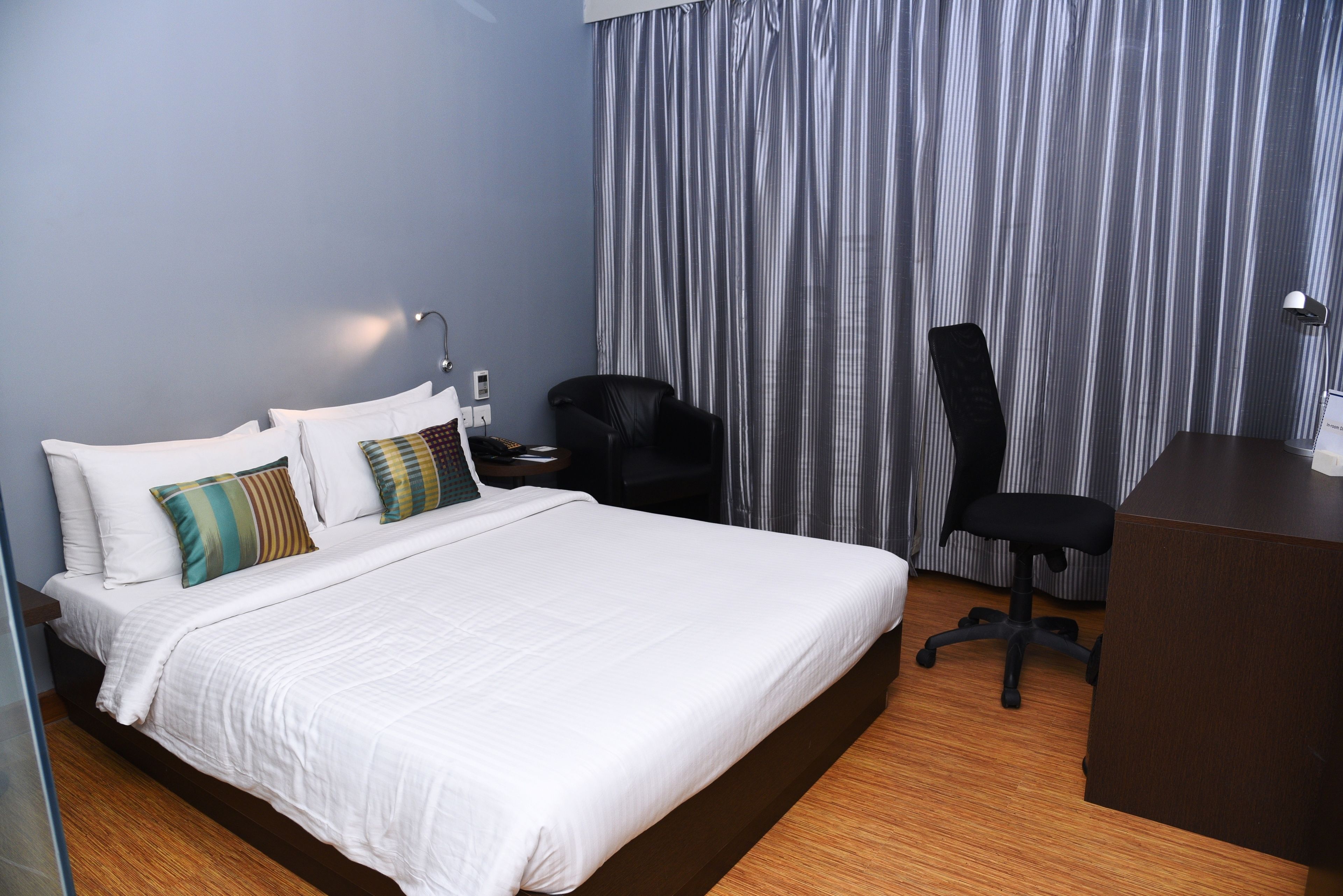 A hotel room with a large bed, a desk, a chair, and a curtain.