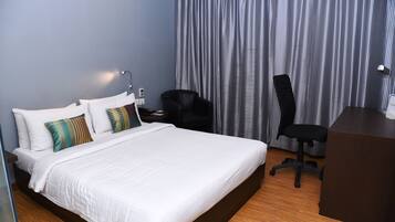 A hotel room with a large bed, a desk, a chair, and a curtain.