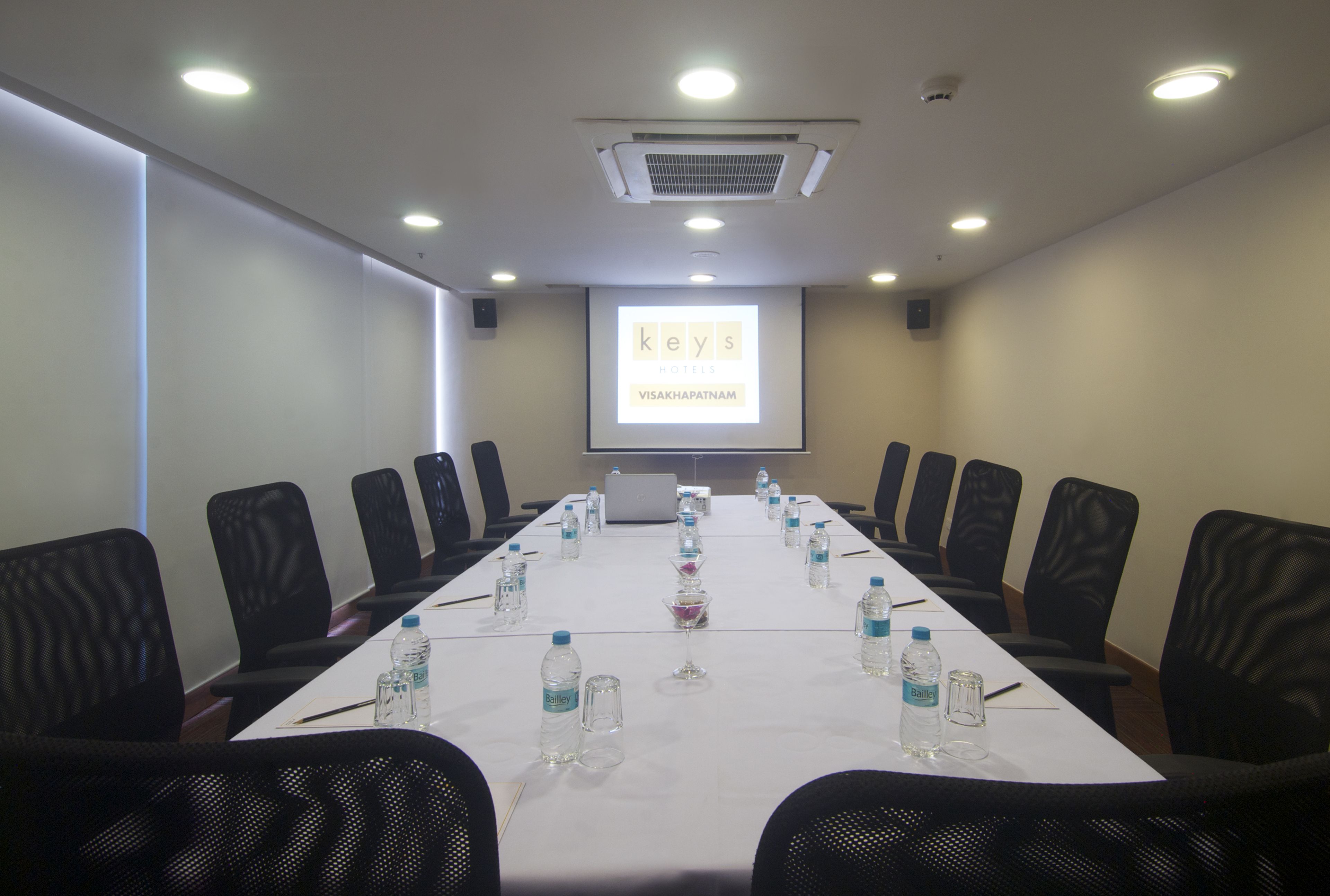 A conference room with a long table, black chairs, water bottles, and a laptop.