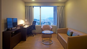 A hotel room with a large window, a desk with a computer, a chair, and a sofa.