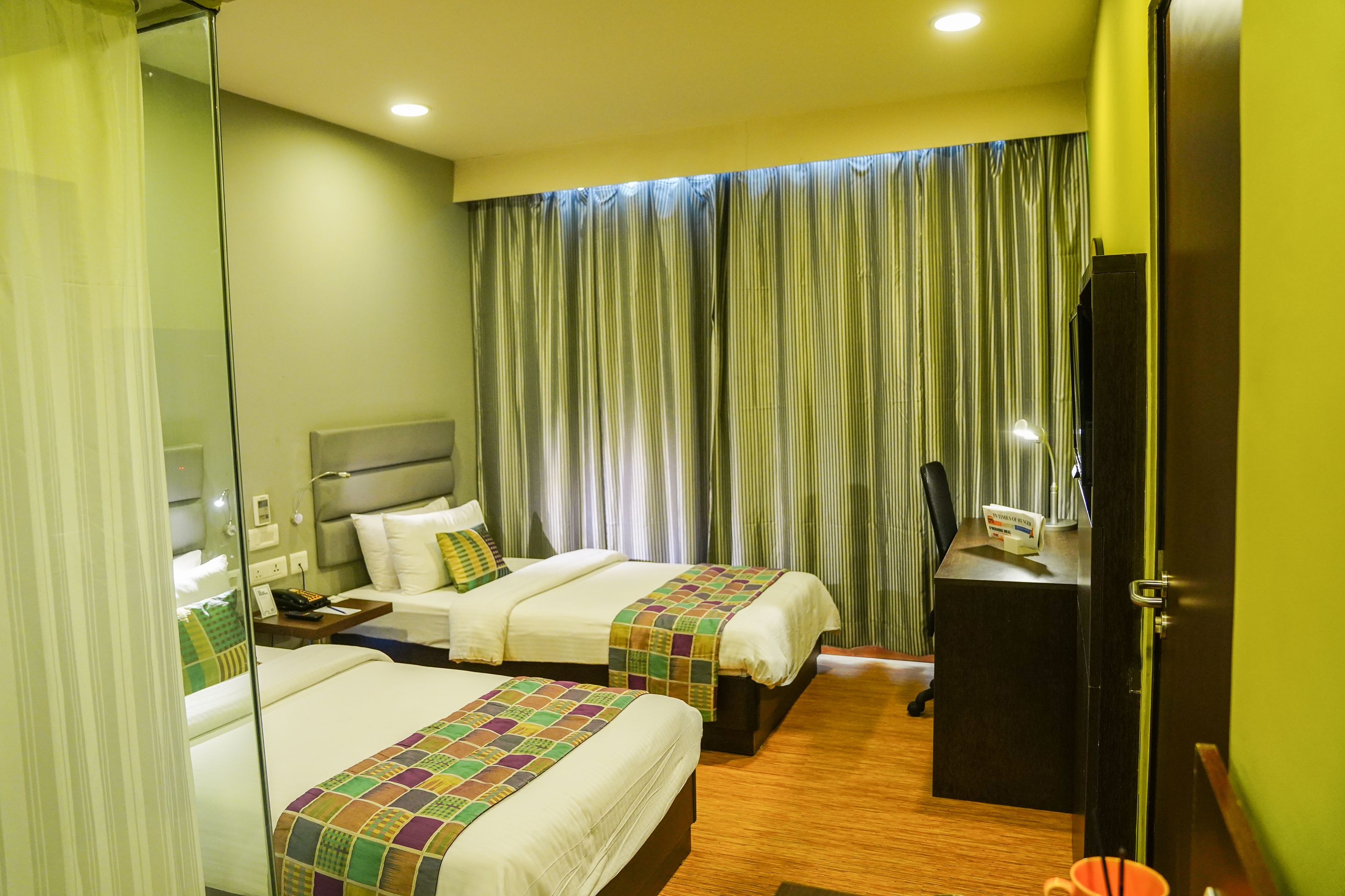 A hotel room with two beds, a desk, a mirror, and a curtain.