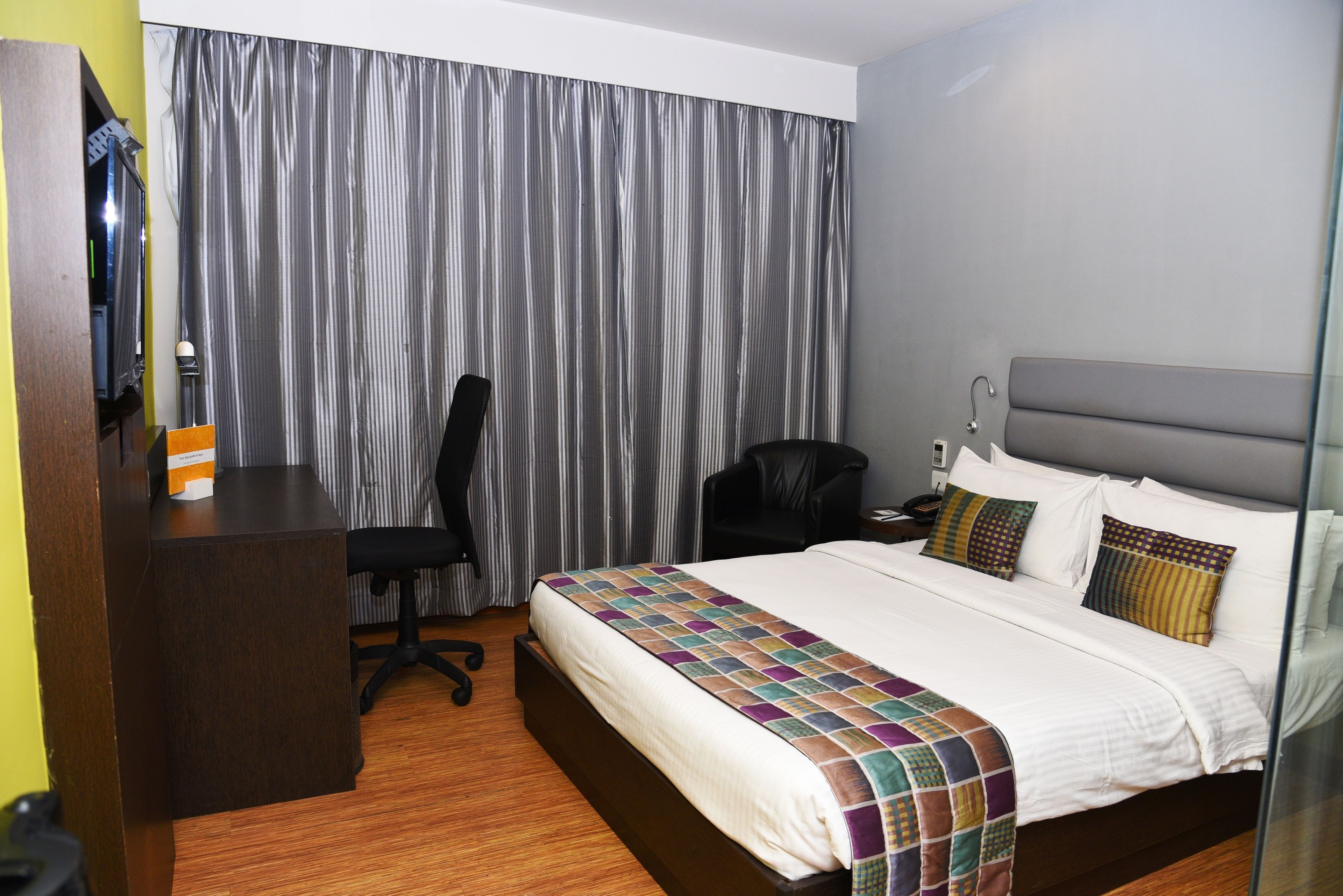 Una habitación de hotel con cama, escritorio, silla y cortina.