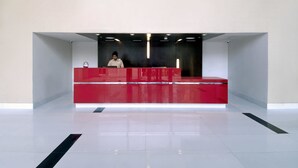 A modern reception desk with a red finish, a person seated behind it, and a clean, tiled floor.
