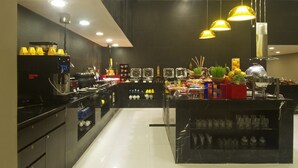 A modern kitchen with black countertops, stainless steel appliances, and yellow pendant lighting.