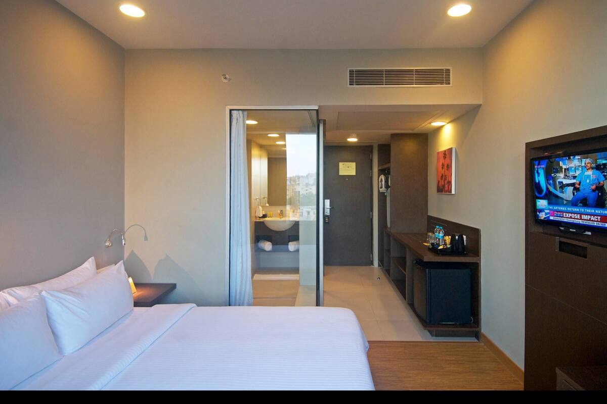 A hotel room with a bed, a television, a desk, and a bathroom visible through an open door.